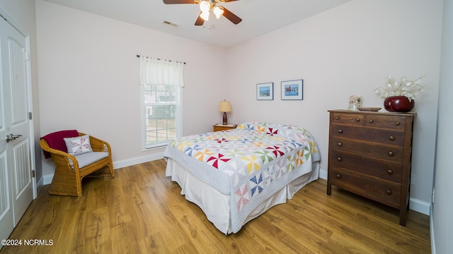 bedroom with a ceiling fan, baseboards, visible vents, and wood finished floors