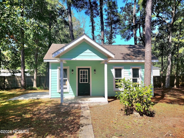 bungalow-style home featuring covered porch, roof with shingles, and fence