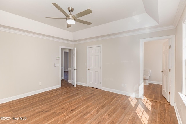 unfurnished bedroom with baseboards, crown molding, a tray ceiling, and wood finished floors