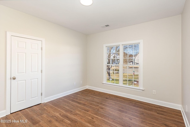 unfurnished room featuring visible vents, dark wood finished floors, and baseboards