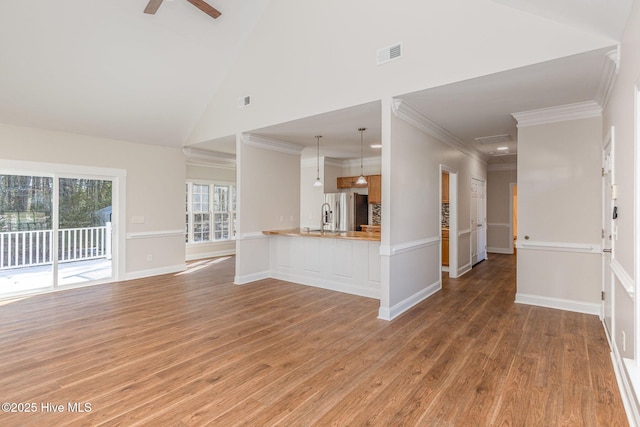 unfurnished living room with ceiling fan, high vaulted ceiling, a sink, wood finished floors, and visible vents