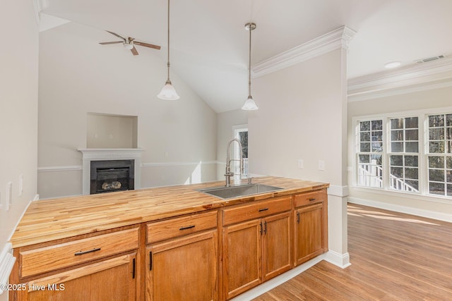 kitchen with a sink, visible vents, open floor plan, hanging light fixtures, and a glass covered fireplace