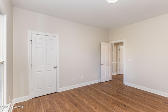 unfurnished bedroom with baseboards and dark wood-style flooring