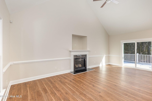 unfurnished living room with a glass covered fireplace, ceiling fan, wood finished floors, high vaulted ceiling, and baseboards