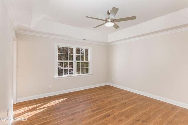 spare room featuring a raised ceiling, baseboards, and wood finished floors