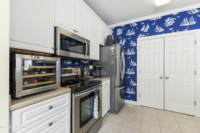 kitchen with wallpapered walls, light tile patterned floors, white cabinets, ornamental molding, and stainless steel appliances