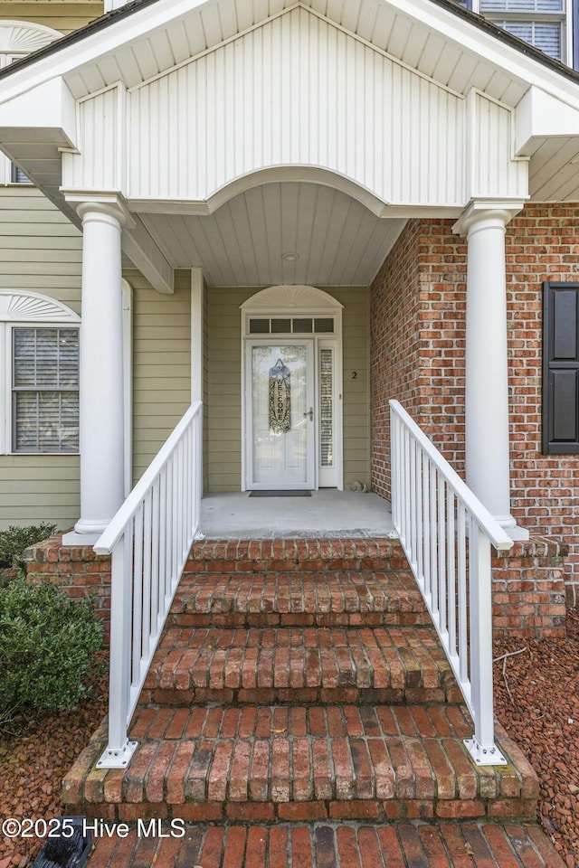 view of exterior entry with a porch and brick siding