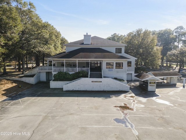 back of house with a porch, concrete driveway, and a chimney