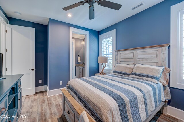 bedroom featuring a barn door, wood finished floors, visible vents, baseboards, and a ceiling fan