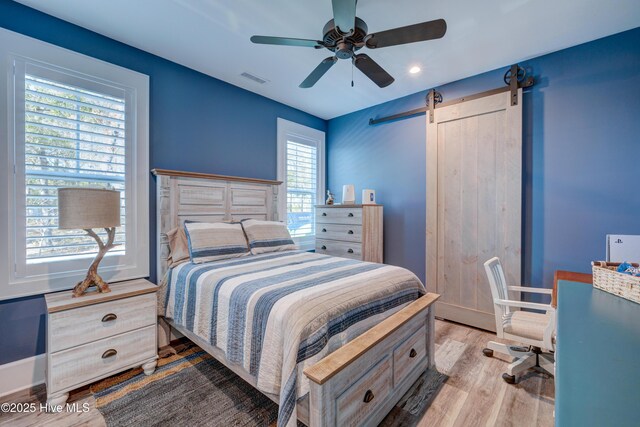 bedroom with a barn door, wood finished floors, visible vents, a ceiling fan, and vaulted ceiling