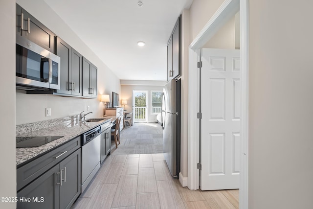 kitchen featuring stainless steel appliances, light stone counters, and a sink