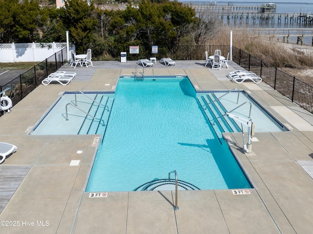 pool with a water view, a patio area, and fence