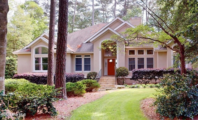 single story home with a chimney, stucco siding, a front yard, and roof with shingles