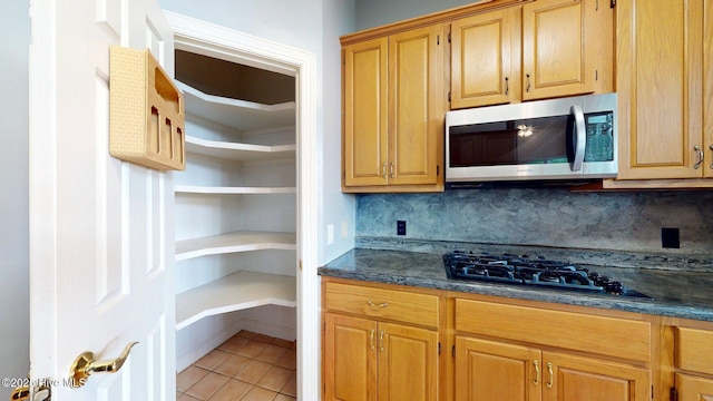 kitchen with stainless steel microwave, black gas stovetop, light tile patterned flooring, open shelves, and backsplash