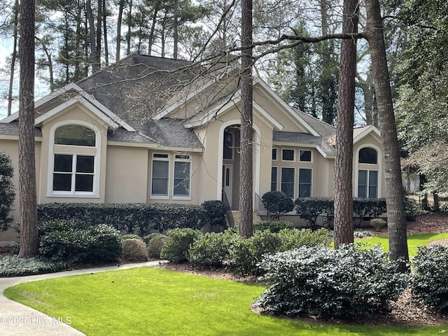 view of front of property featuring a front yard, roof with shingles, and stucco siding