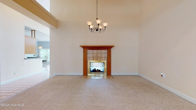unfurnished living room featuring baseboards, an inviting chandelier, light carpet, a fireplace, and a towering ceiling