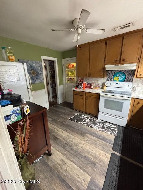 kitchen with brown cabinetry, white appliances, visible vents, and under cabinet range hood