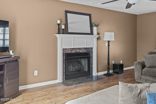 living room featuring a ceiling fan, baseboards, wood finished floors, and a high end fireplace