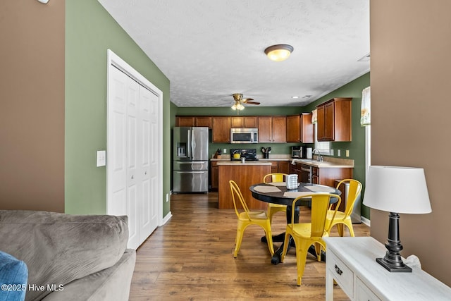 kitchen with light countertops, appliances with stainless steel finishes, a sink, a kitchen island, and wood finished floors