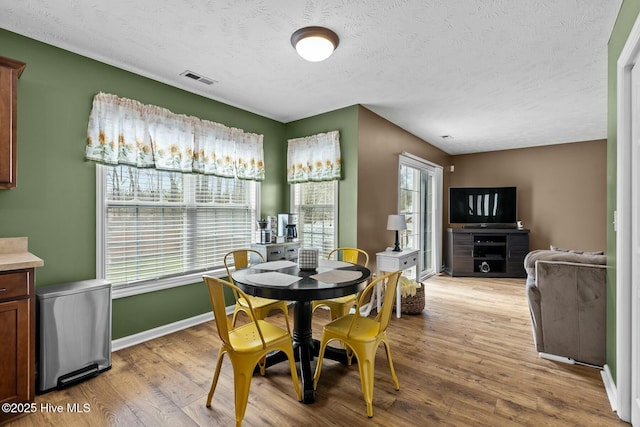 dining space with visible vents, a textured ceiling, light wood-style flooring, and baseboards