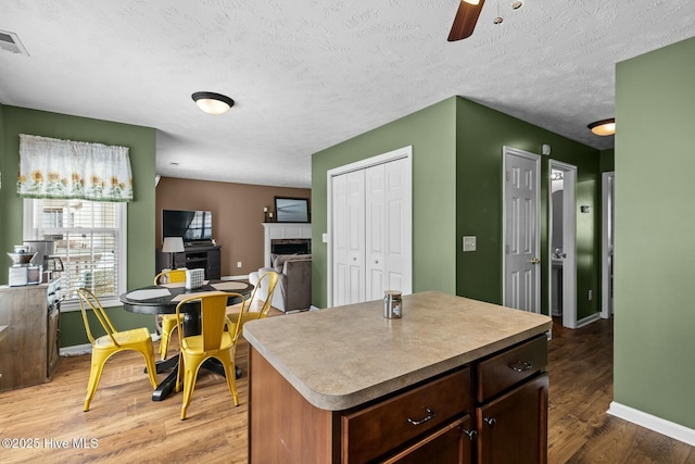 kitchen with baseboards, a tile fireplace, light wood-style flooring, ceiling fan, and a center island