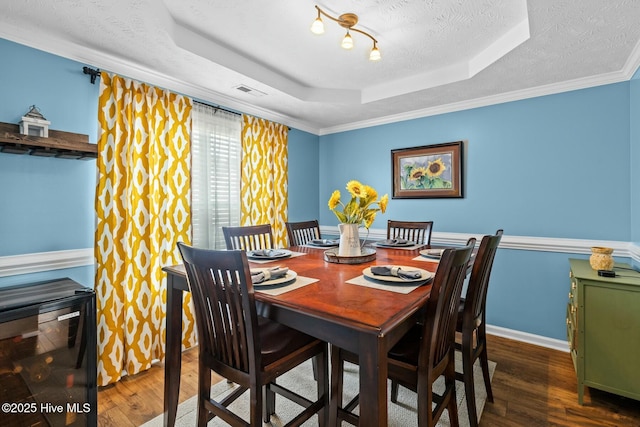 dining area with a raised ceiling, visible vents, a textured ceiling, and wood finished floors