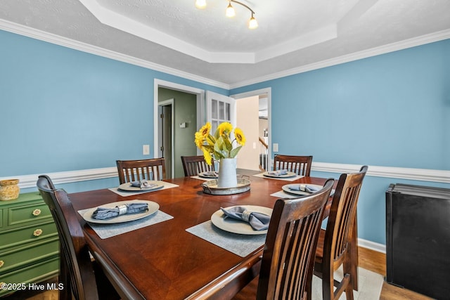 dining space with a textured ceiling, a tray ceiling, and wood finished floors