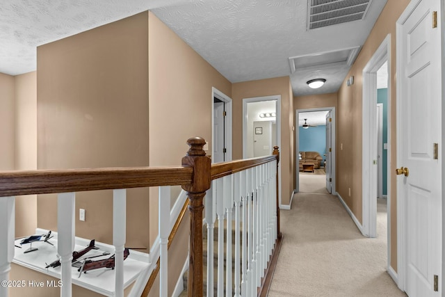 corridor with light carpet, a textured ceiling, visible vents, and attic access