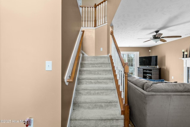 stairs featuring a fireplace, a textured ceiling, and ceiling fan