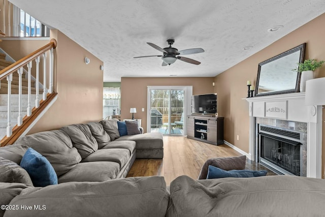 living area featuring ceiling fan, a fireplace, wood finished floors, baseboards, and stairway