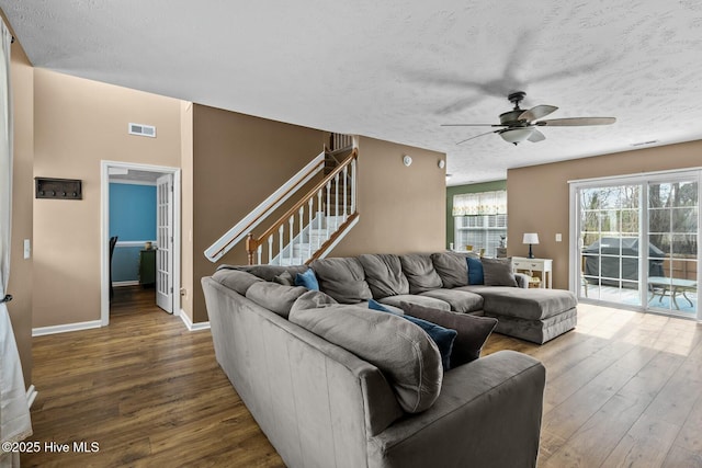 living room featuring visible vents, stairway, a textured ceiling, wood finished floors, and baseboards