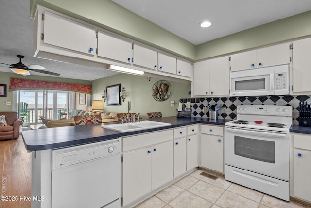 kitchen featuring white appliances, white cabinets, dark countertops, open floor plan, and a sink