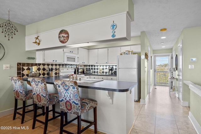 kitchen with dark countertops, white cabinetry, white appliances, a peninsula, and a kitchen bar