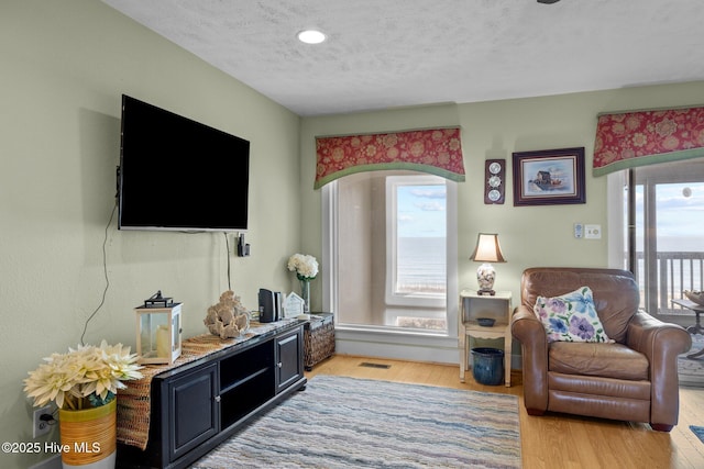 living room featuring light wood-type flooring, plenty of natural light, visible vents, and a textured ceiling