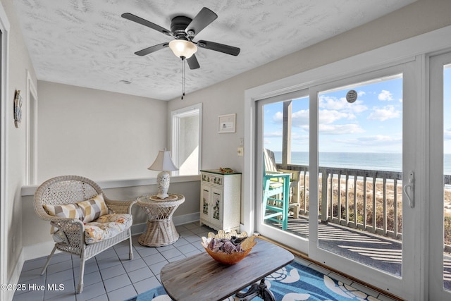 living area featuring a water view, baseboards, a textured ceiling, and light tile patterned flooring