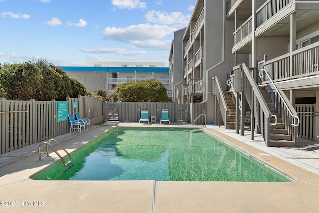 community pool featuring a patio area, a water view, fence, and stairs