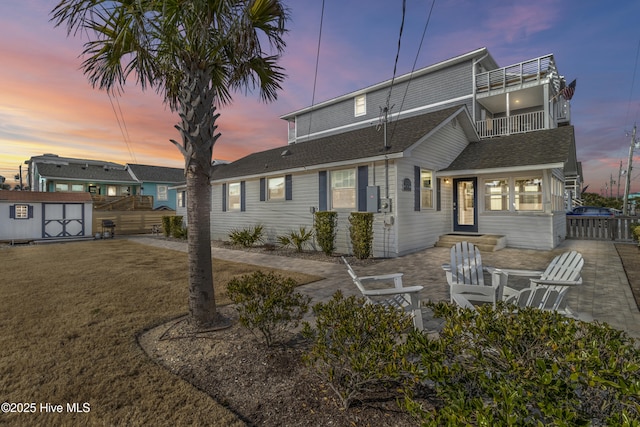 back of property at dusk with an outbuilding, roof with shingles, fence, a balcony, and a shed