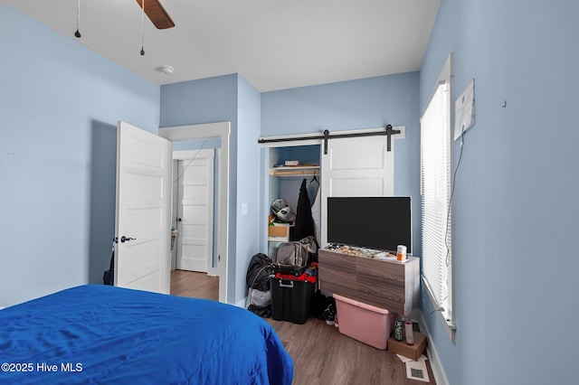 bedroom with a ceiling fan, wood finished floors, visible vents, a closet, and a barn door