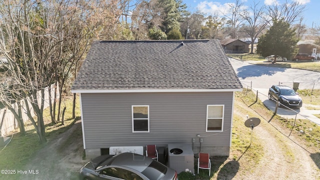 back of house with central AC unit and roof with shingles