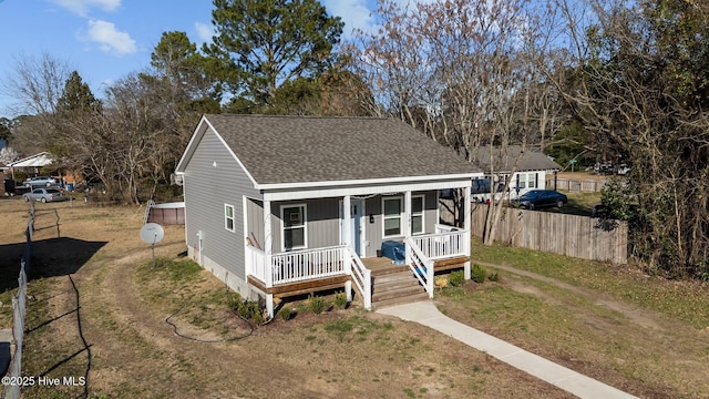 view of front facade with a front yard, fence, covered porch, and roof with shingles