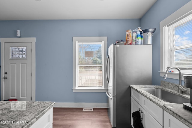 kitchen featuring visible vents, a sink, wood finished floors, freestanding refrigerator, and white cabinets