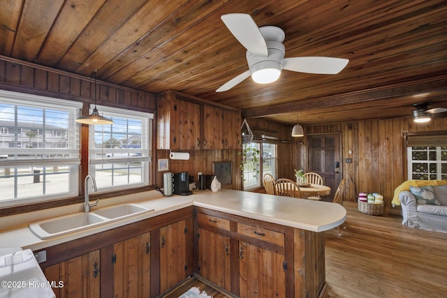 kitchen with brown cabinetry, wooden ceiling, a peninsula, light countertops, and a sink