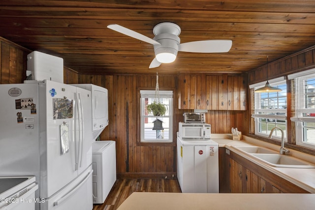 kitchen with stacked washer and dryer, light countertops, a sink, wood walls, and white appliances