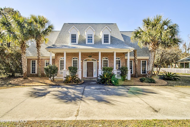 cape cod home with a porch, brick siding, and a shingled roof