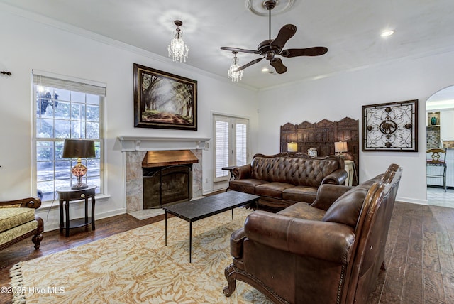 living room featuring baseboards, arched walkways, a tile fireplace, dark wood-style flooring, and crown molding