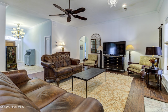 living area with arched walkways, crown molding, light wood-type flooring, baseboards, and ceiling fan with notable chandelier