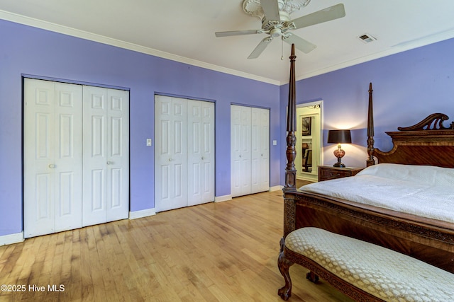 bedroom with multiple closets, light wood-style flooring, visible vents, and crown molding