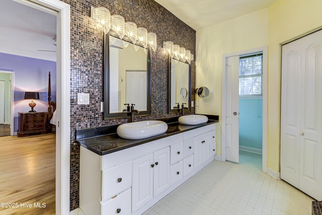 ensuite bathroom with double vanity, ensuite bath, tasteful backsplash, and a sink