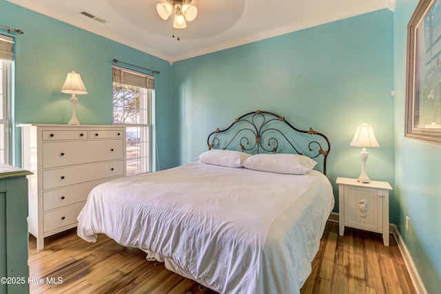 bedroom featuring visible vents, baseboards, light wood-style flooring, ceiling fan, and ornamental molding