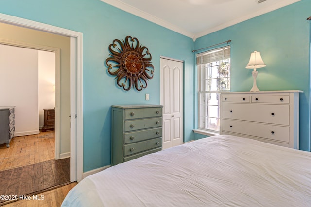 bedroom featuring visible vents, baseboards, light wood-style floors, ornamental molding, and a closet